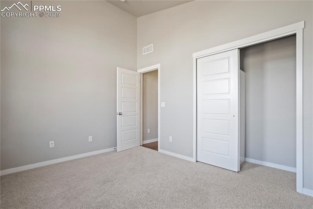 Image 30 of 50: main level guest bedroom featuring a towering ceiling, light carpet, and a 