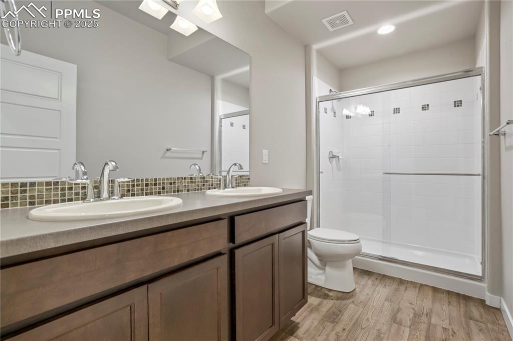 Image 44 of 50: Bathroom featuring double vanity, light wood-style floors, and a stall show