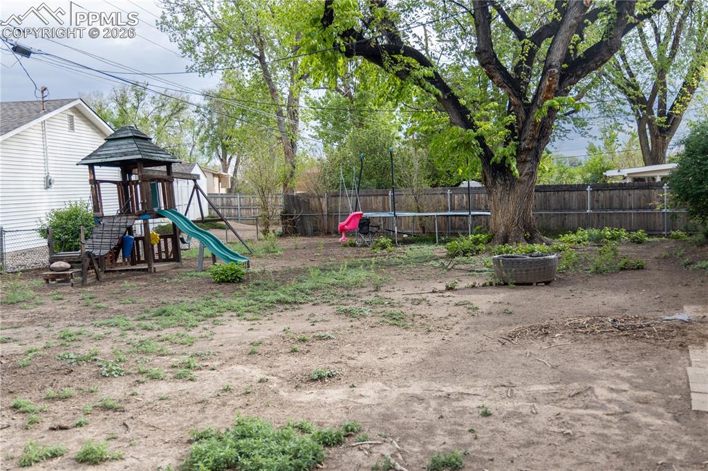 Image 12 of 12: Fenced backyard with a trampoline and a playground