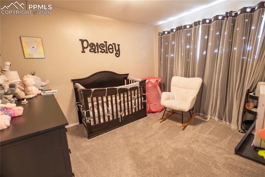 Image 8 of 11: Bedroom with light colored carpet and a crib