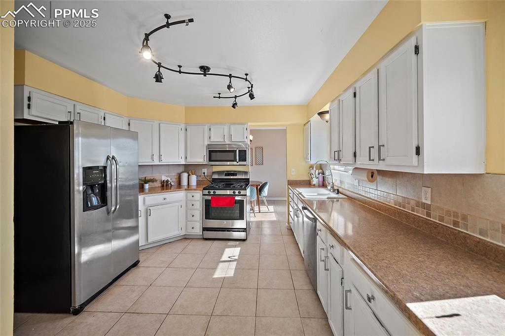 Image 12 of 45: Kitchen featuring stainless steel appliances, white cabinets, light tile pa