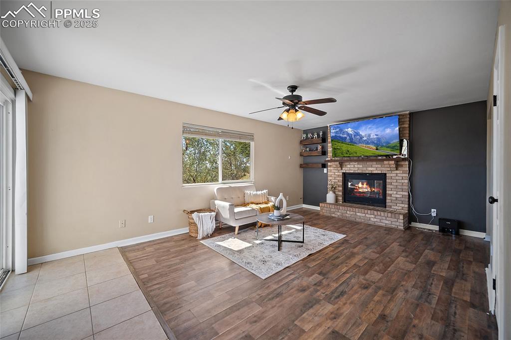 Image 17 of 45: Living room featuring ceiling fan, a brick fireplace, and wood finished flo