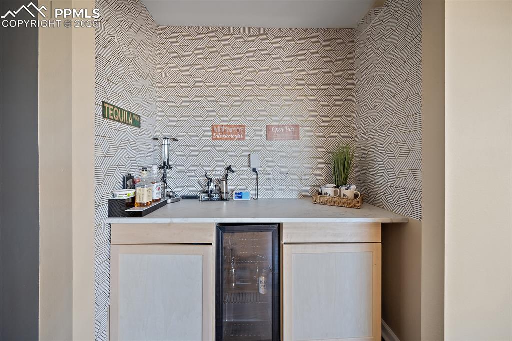 Image 22 of 45: Indoor dry bar with light brown cabinets, wine cooler, light stone countert