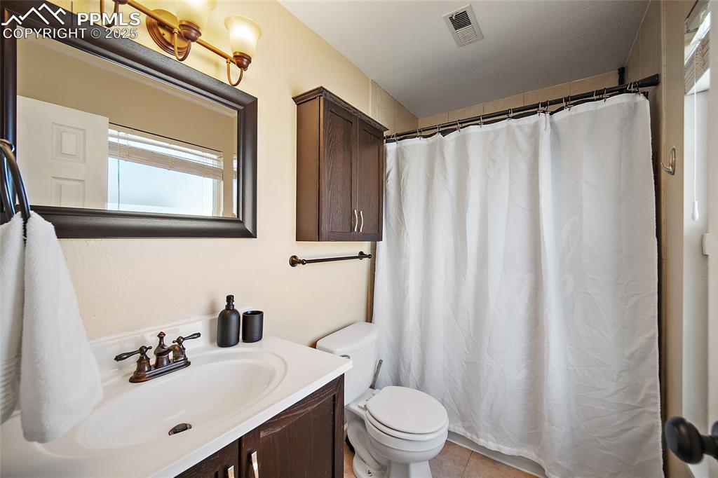 Image 25 of 45: Full bath with vanity, light tile patterned floors, and a shower with showe