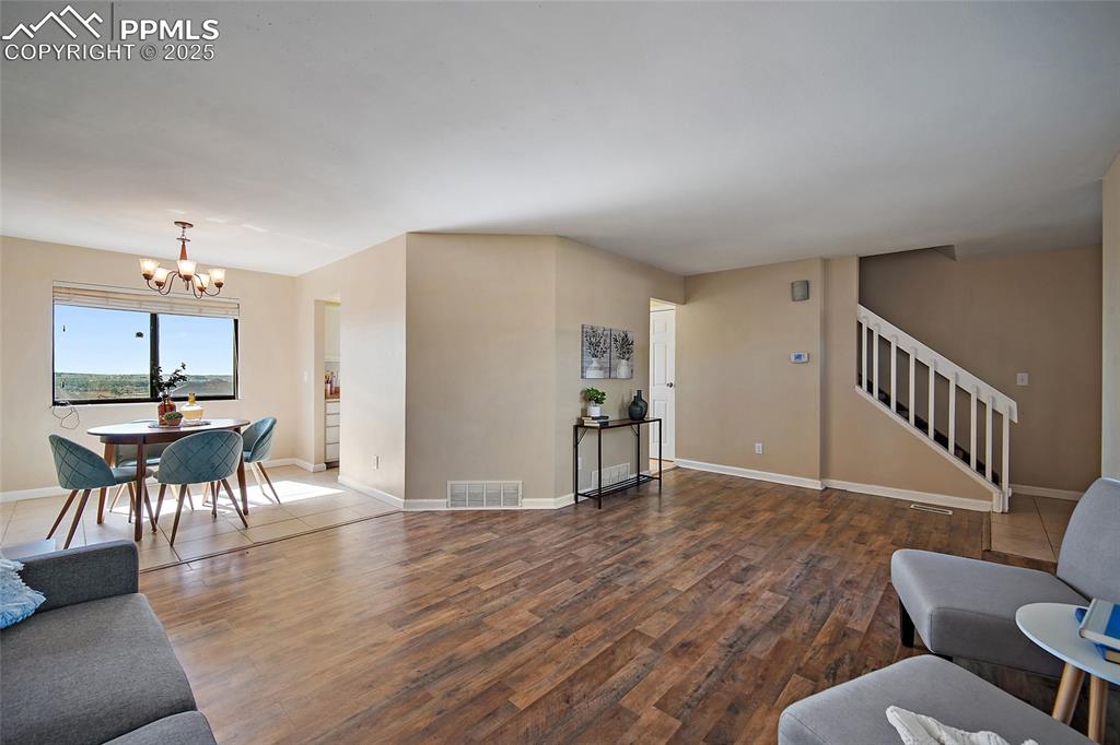 Image 8 of 45: Living room with wood finished floors, a chandelier, and stairway
