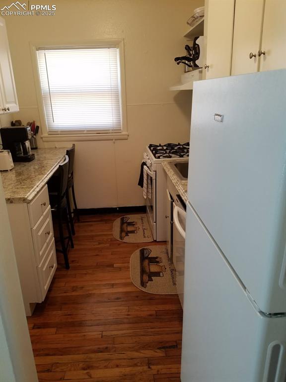 Image 12 of 25: Kitchen featuring white appliances, dark wood-style flooring, white cabinet