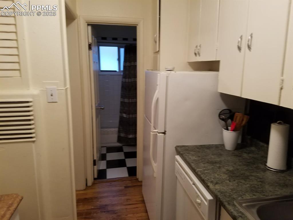 Image 21 of 25: Kitchen featuring white cabinetry, dishwasher, dark countertops, and wood f