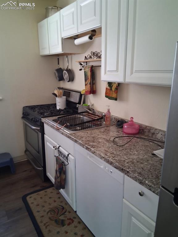Image 22 of 25: Kitchen with stainless steel appliances, white cabinets, dark wood finished