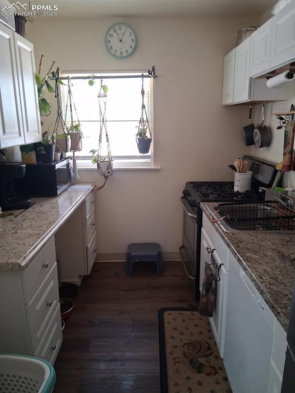 Image 23 of 25: Kitchen with stainless steel gas range, dark wood-type flooring, white cabi