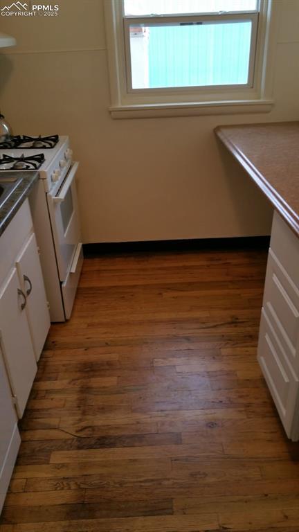 Image 9 of 25: Kitchen featuring white gas range oven, wood finished floors, white cabinet
