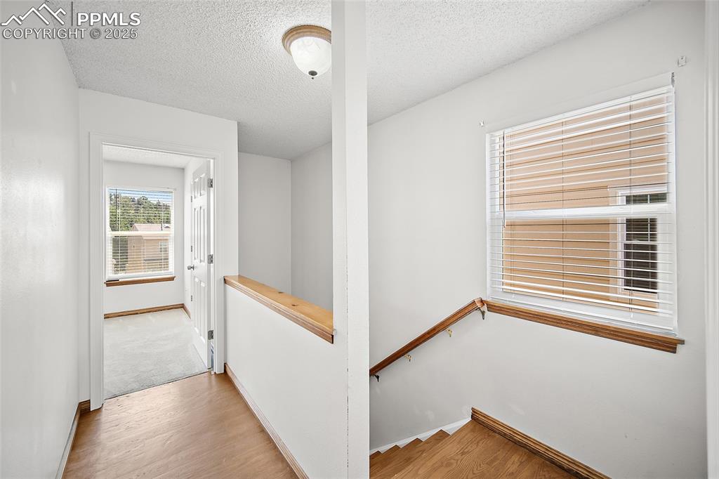 Image 19 of 41: Hall featuring an upstairs landing, a textured ceiling, and wood finished f