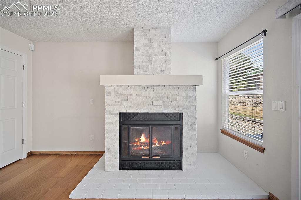 Image 8 of 41: Detailed view of wood finished floors, a stone fireplace, and a textured ce