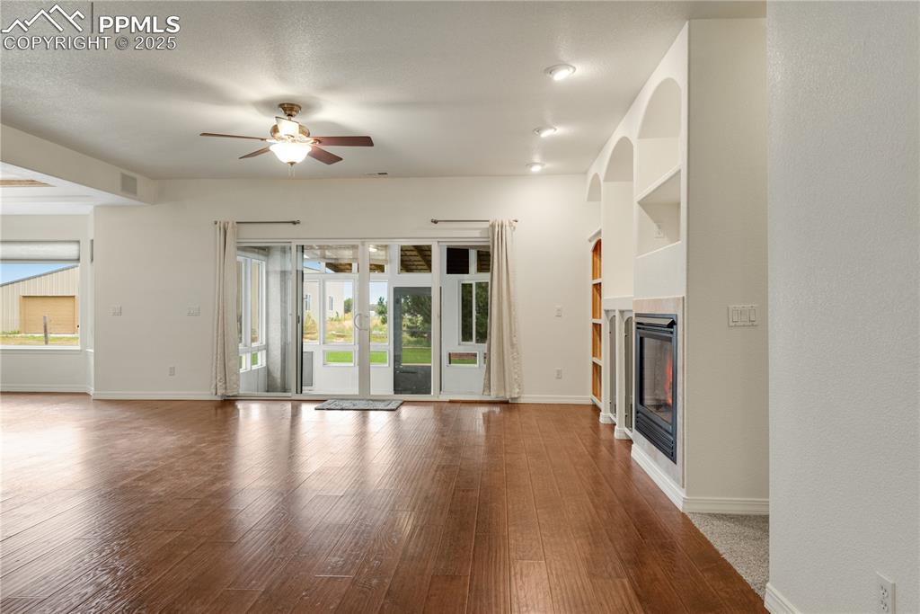 Image 16 of 48: Unfurnished living room with wood-type flooring, a fireplace, a ceiling fan