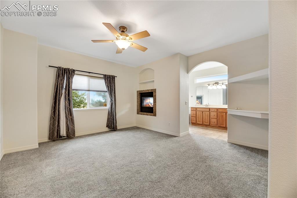 Image 24 of 48: Unfurnished living room with light carpet, a ceiling fan, and built in shel