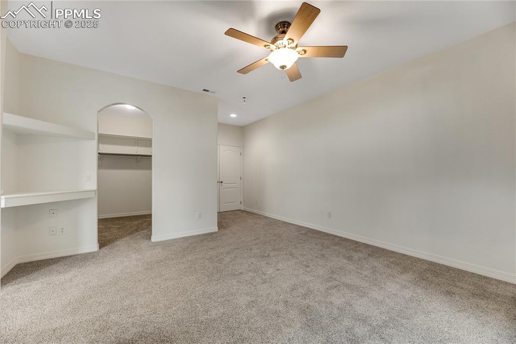 Image 25 of 48: Unfurnished bedroom with a walk in closet, light carpet, ceiling fan, and a