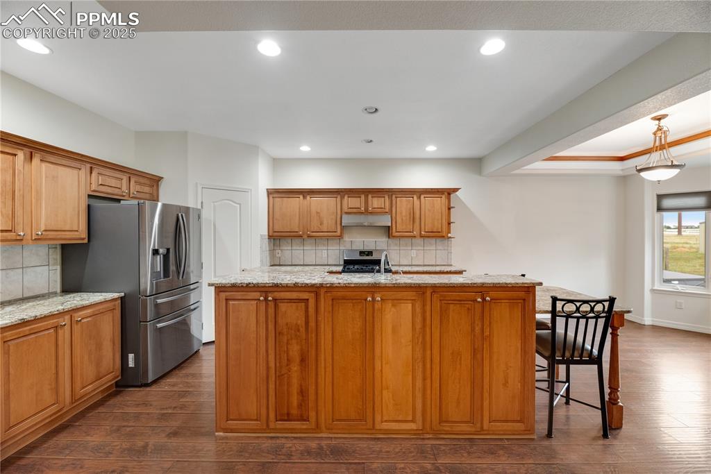 Image 38 of 48: Kitchen with a kitchen island with sink, light stone counters, tasteful bac
