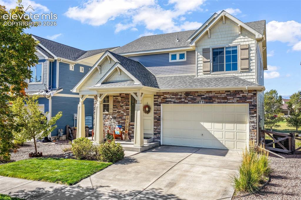 Caption: Two-story residence featuring a covered front porch, stone and siding exterior, attached garage, and
