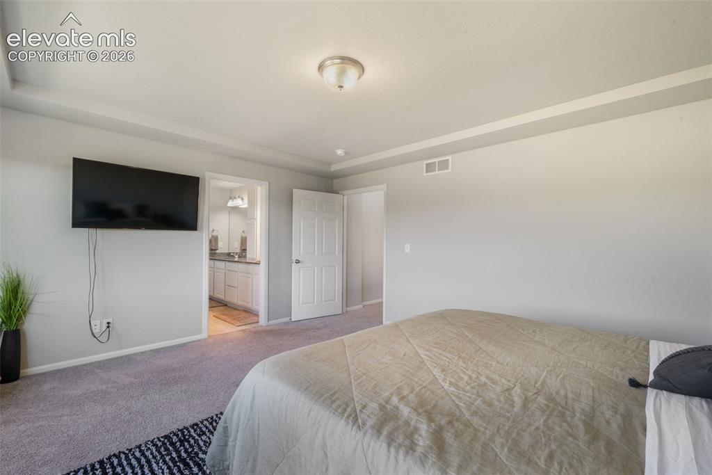 Image 26 of 48: Tray ceiling with recessed lighting, wall-mounted television, and a bathroo