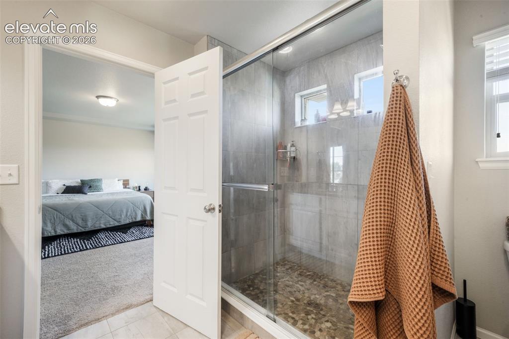 Image 28 of 48: Glass-enclosed shower with tiled walls and a pebble-finish floor