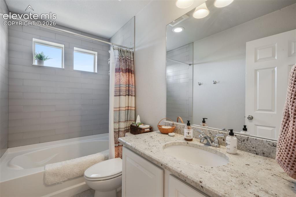 Image 35 of 48: White bathtub with light gray tile surround, two transom windows, and a bui