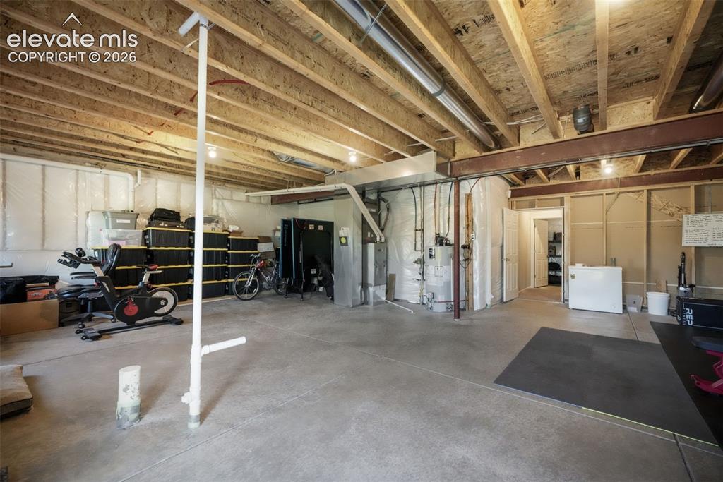Image 38 of 48: Unfinished basement featuring exposed wood joists, concrete flooring, and a