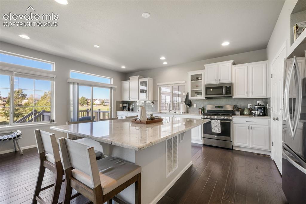 Image 7 of 48: Kitchen featuring a large central island with seating, white shaker-style c