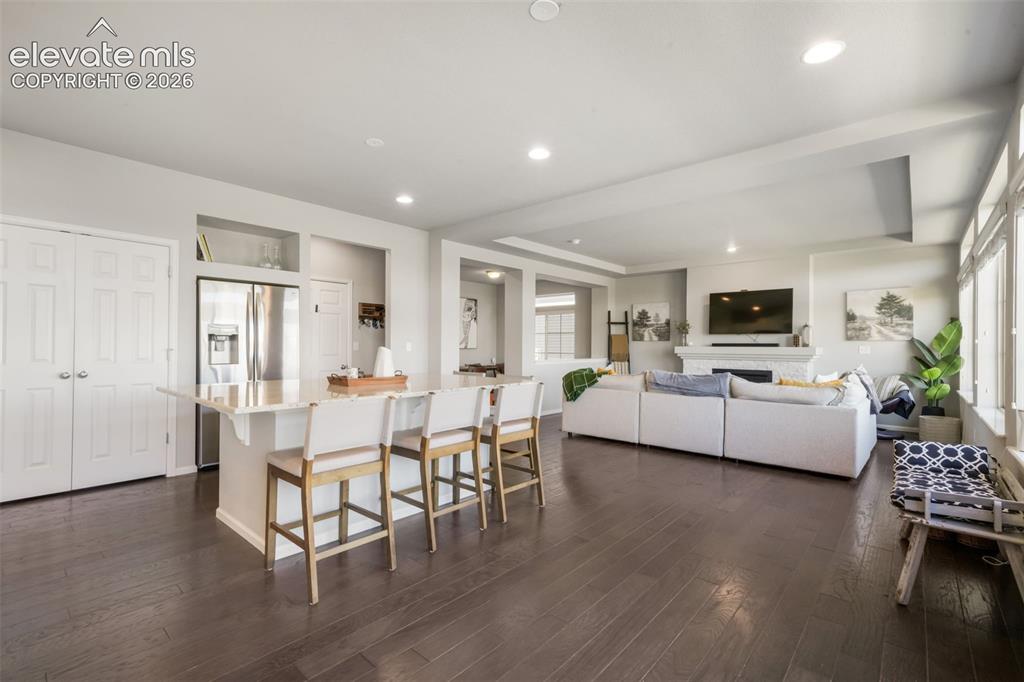 Image 9 of 48: Kitchen island with stone countertop, stainless steel refrigerator, dark wo