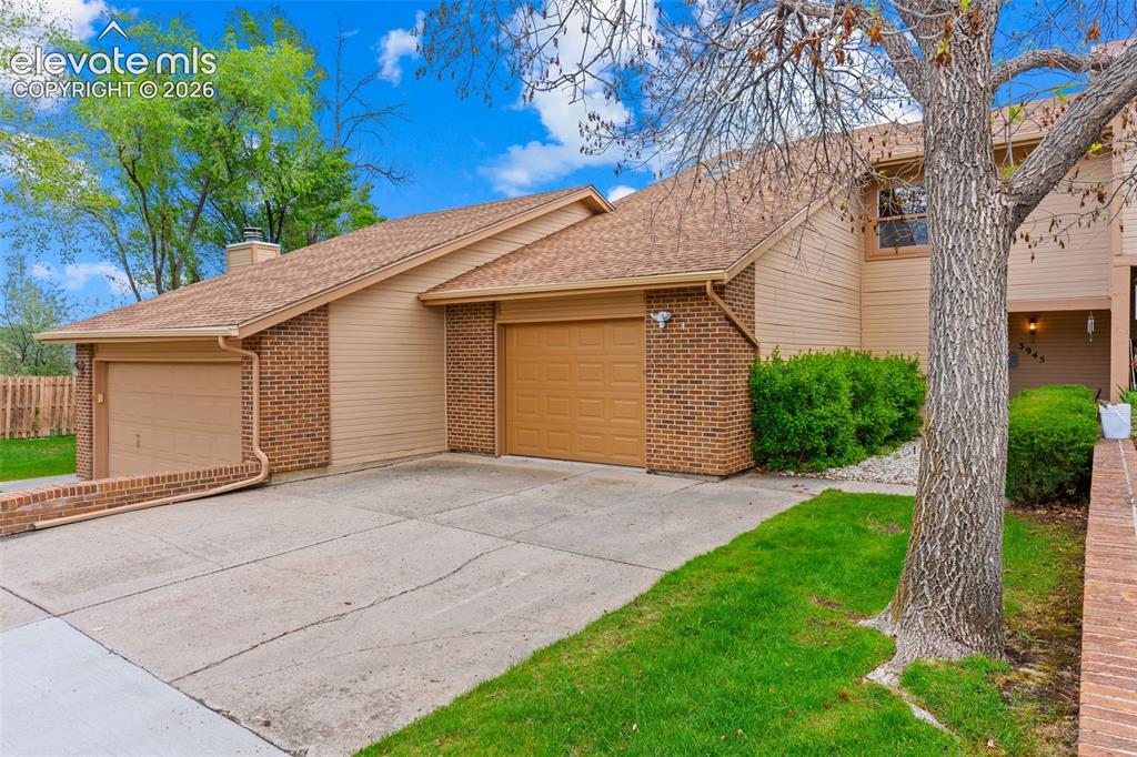 Image 2 of 32: Tan siding and brick exterior featuring a two-car garage, concrete driveway