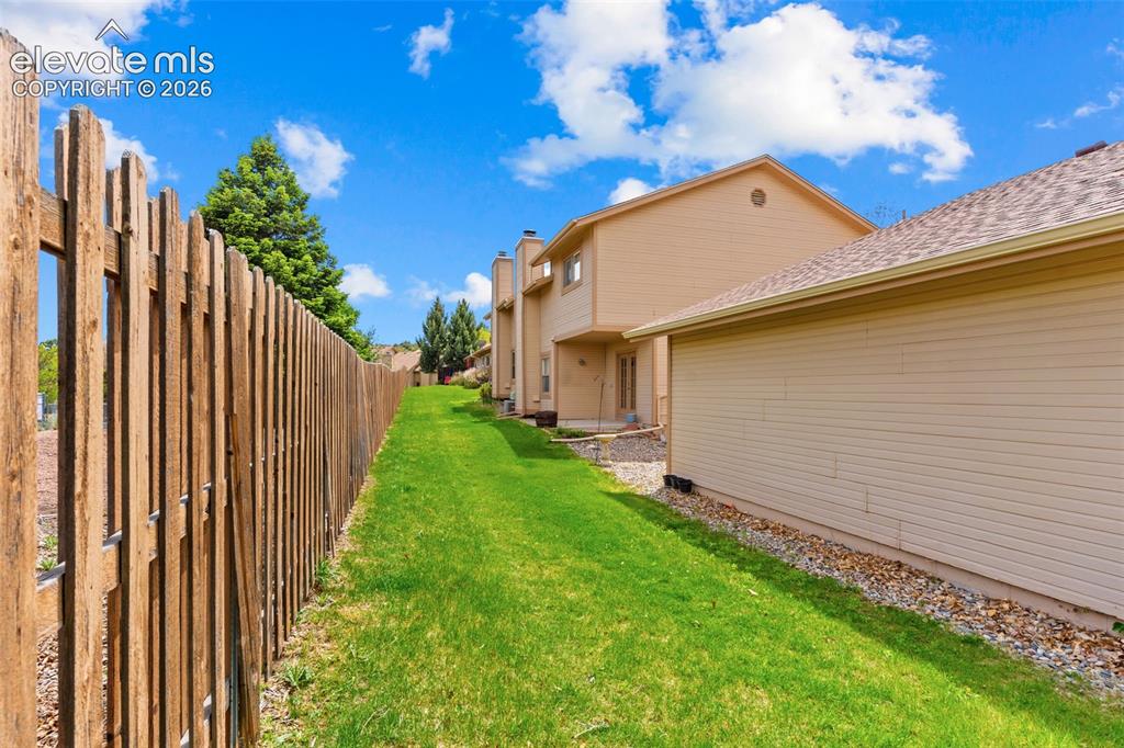 Image 28 of 32: Expansive green space featuring a wood fence, mature evergreen trees, and a