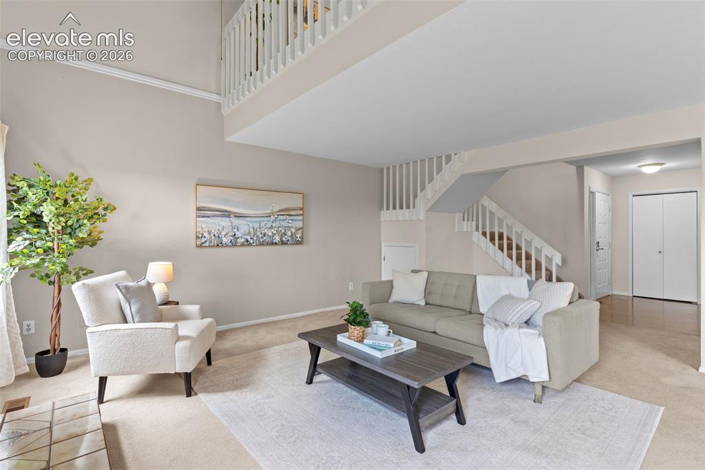Image 8 of 32: Spacious living area featuring a two-story ceiling, a staircase with white 