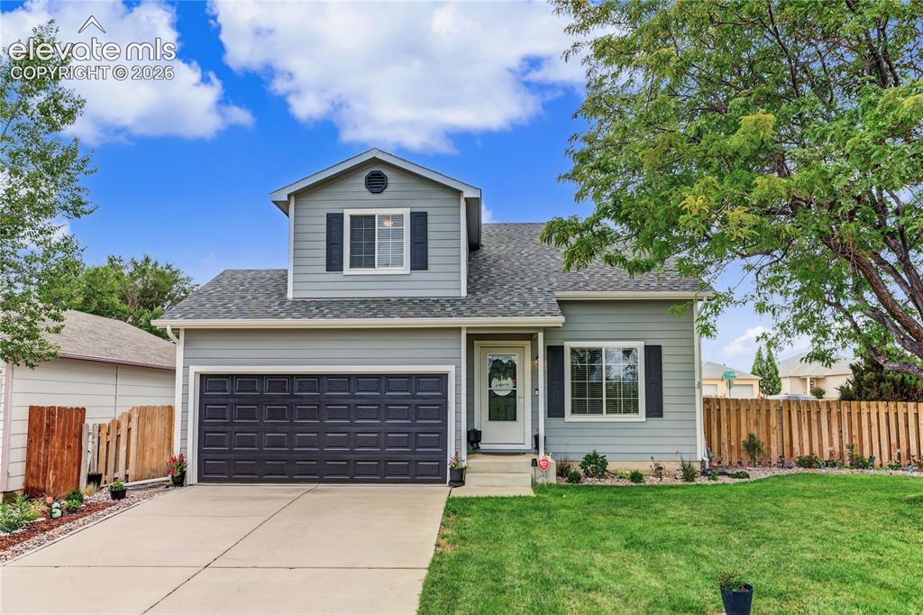 Caption: Two-story residence with a two-car garage, gray siding, and black window shutters
