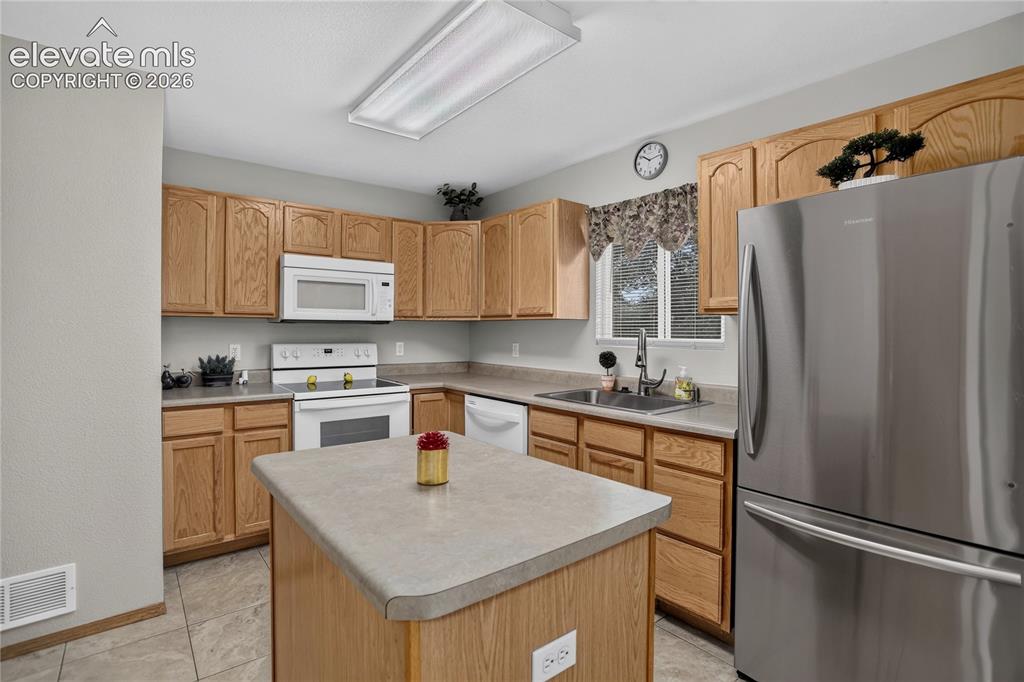 Image 13 of 36: Kitchen featuring wood cabinetry, white appliances, a center island with co