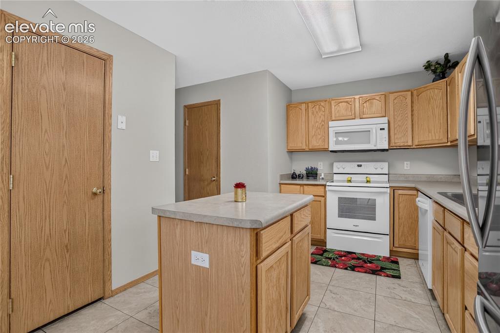 Image 15 of 36: Kitchen featuring light wood cabinetry, white appliances, a center island w