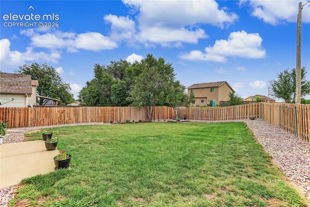Image 33 of 36: Expansive backyard featuring a manicured lawn, full privacy fencing, and a