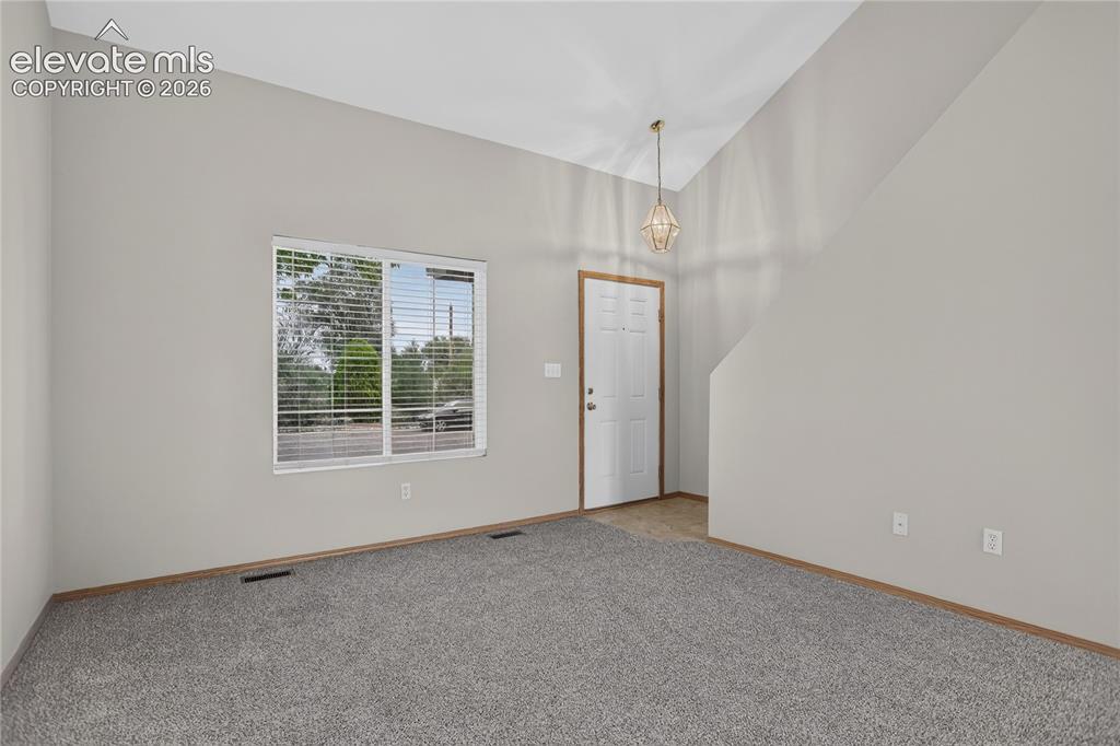 Image 4 of 36: Spacious room with a vaulted ceiling, an entry door, and a large window wit