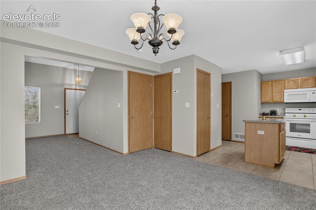 Image 9 of 36: Open living area with neutral gray wall paint, carpeting, and a chandelier