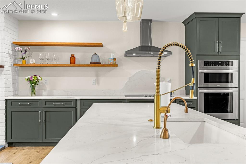 Image 5 of 43: Kitchen featuring green cabinets, light stone counters, wall chimney exhaus