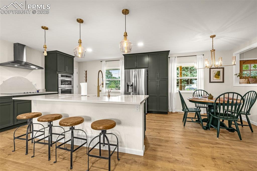 Image 7 of 43: Kitchen featuring pendant lighting, light wood-style flooring, wall chimney