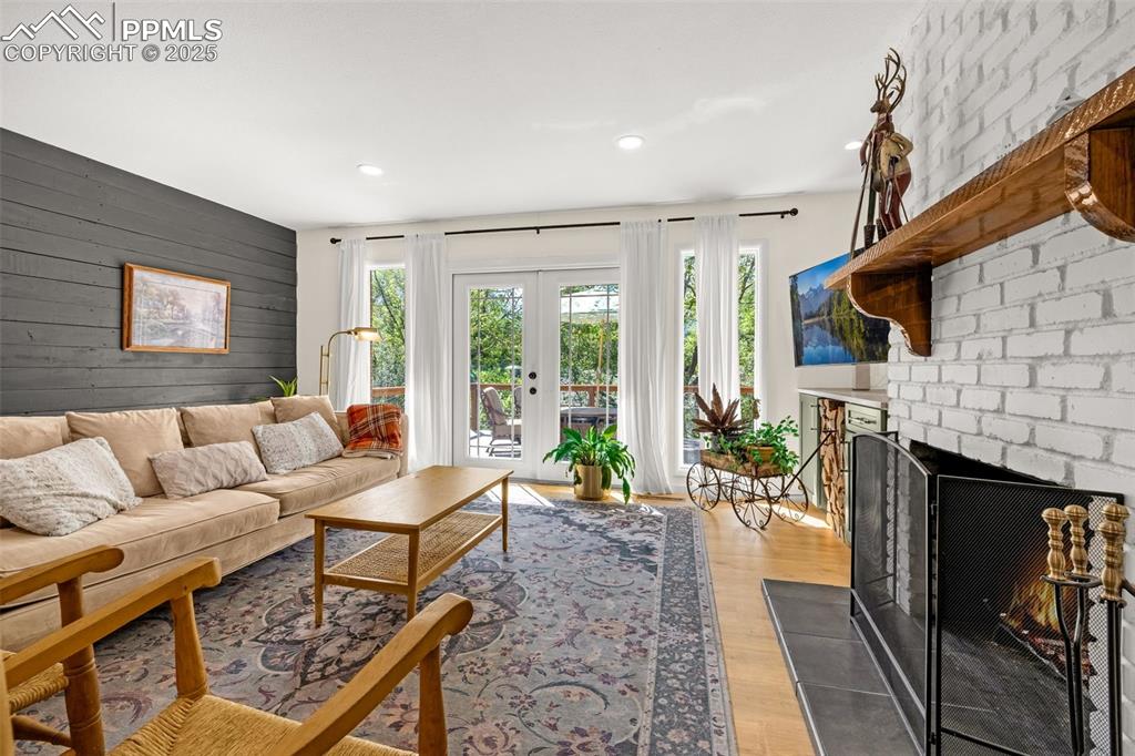 Image 9 of 43: Living room featuring wooden walls, a brick fireplace, french doors, wood f