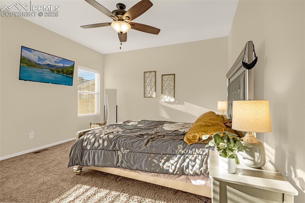 Image 13 of 28: Carpeted bedroom with visible vents, a ceiling fan, and baseboards