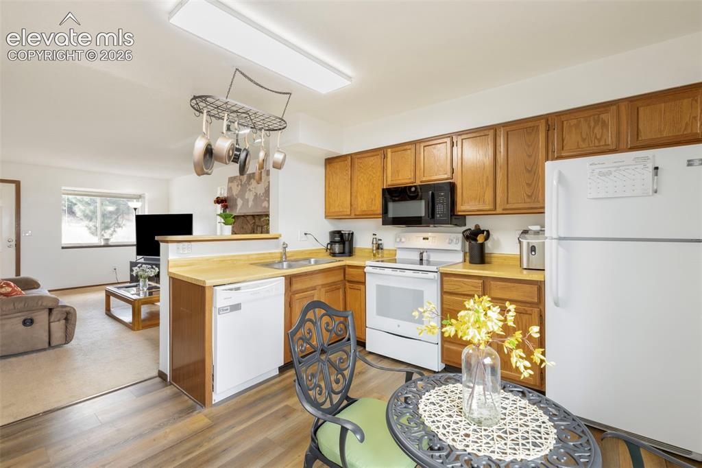 Image 10 of 26: Kitchen featuring wood-finish flooring, wood cabinetry, white appliances, a
