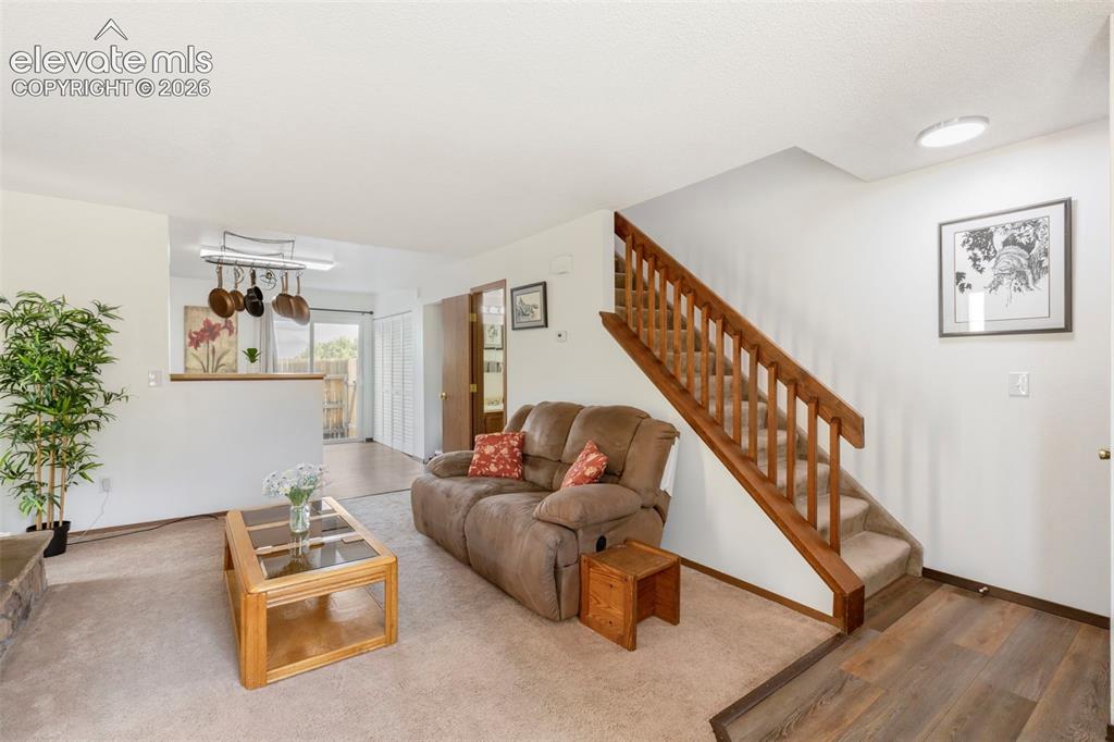 Image 5 of 26: Carpeted living area with a half-wall partition, a wooden staircase, and wo