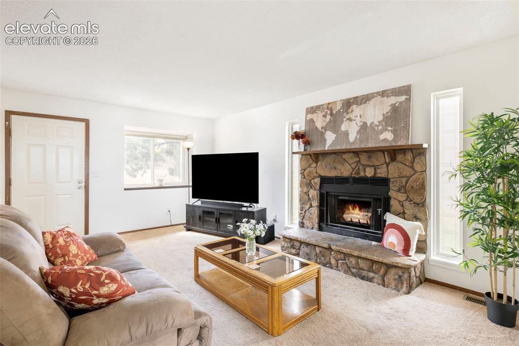 Image 6 of 26: Living room featuring a stone-clad fireplace with a hearth, a substantial w