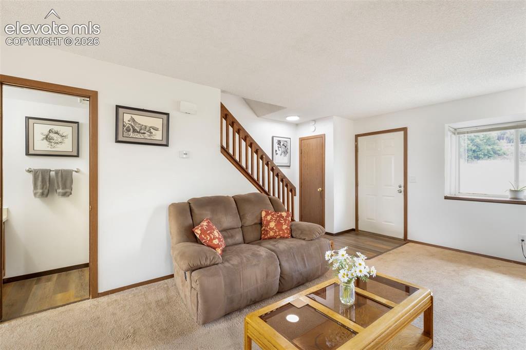 Image 7 of 26: Living area featuring light beige carpeting, white walls, and a wood-finish
