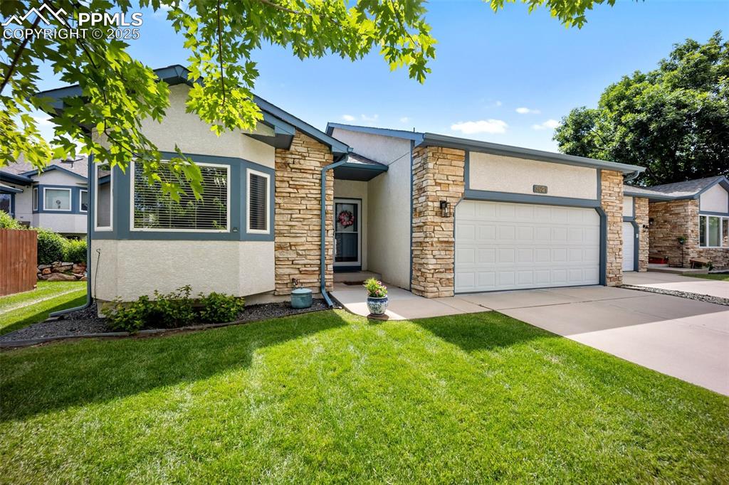 Caption: View of front of house with stucco siding, stone siding, a garage, and driveway