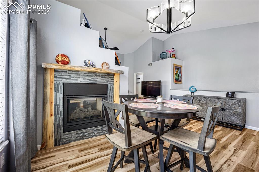 Image 10 of 50: Dining room with a stone fireplace, wood finished floors, a chandelier, and