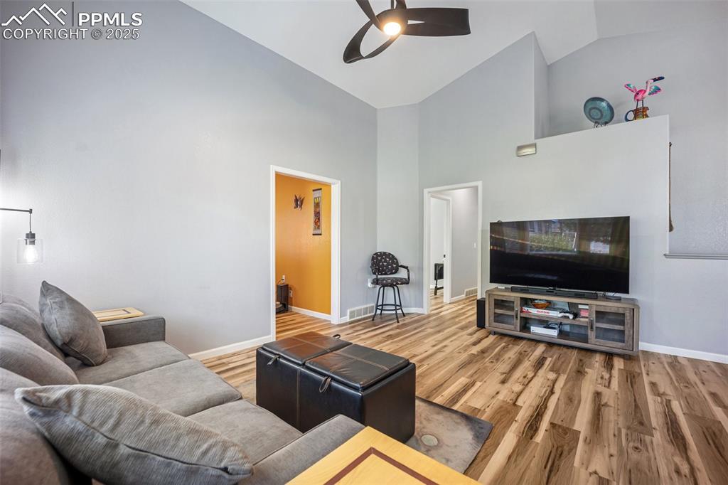 Image 18 of 50: Living room with ceiling fan, high vaulted ceiling, and wood finished floor