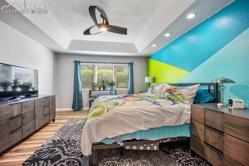 Image 29 of 50: Bedroom with a tray ceiling, light wood finished floors, recessed lighting,