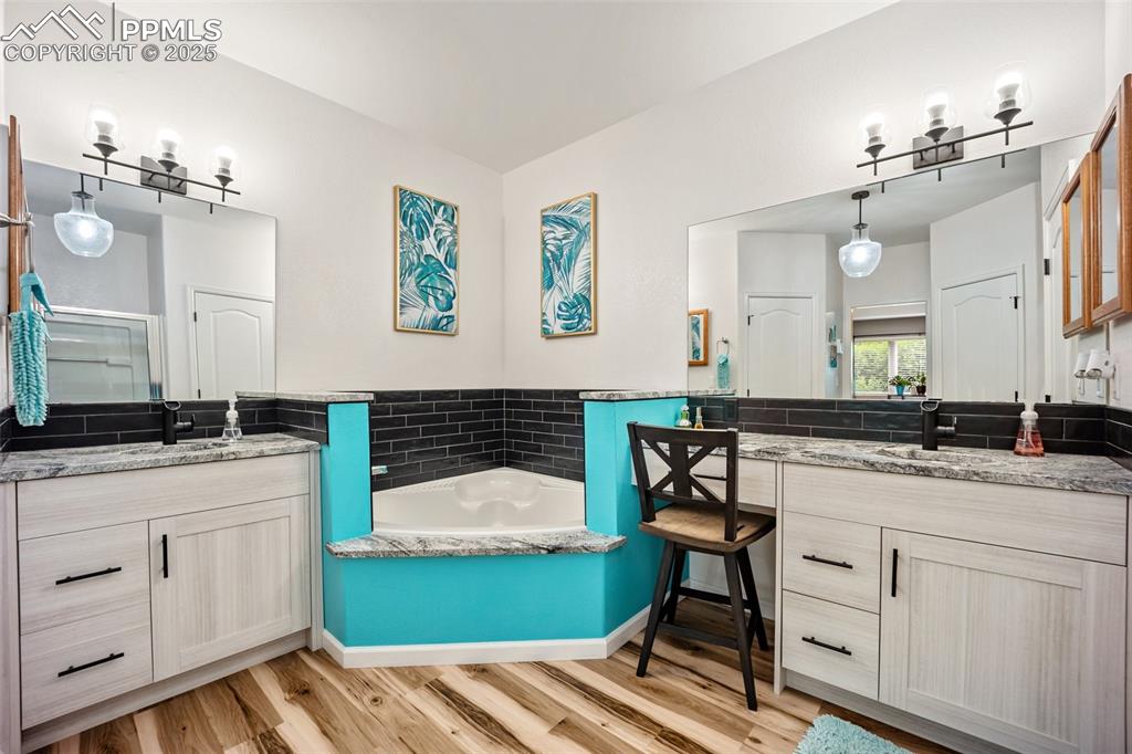 Image 30 of 50: Full bathroom with two vanities, wood finished floors, a garden tub, and a 