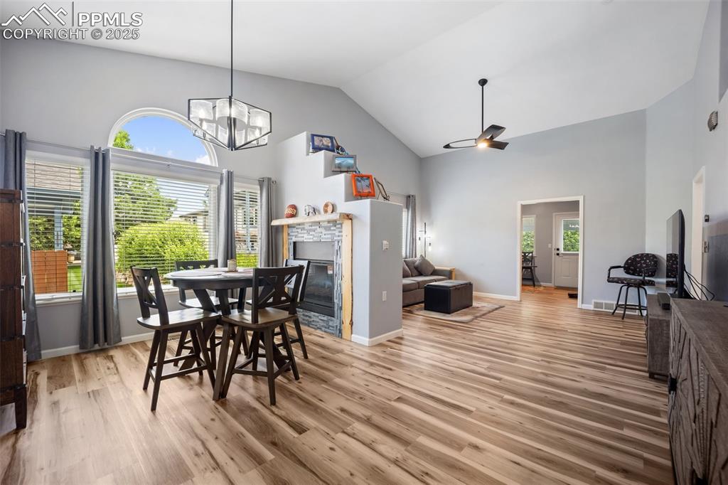 Image 7 of 50: Dining area featuring high vaulted ceiling, light wood-type flooring, a gla